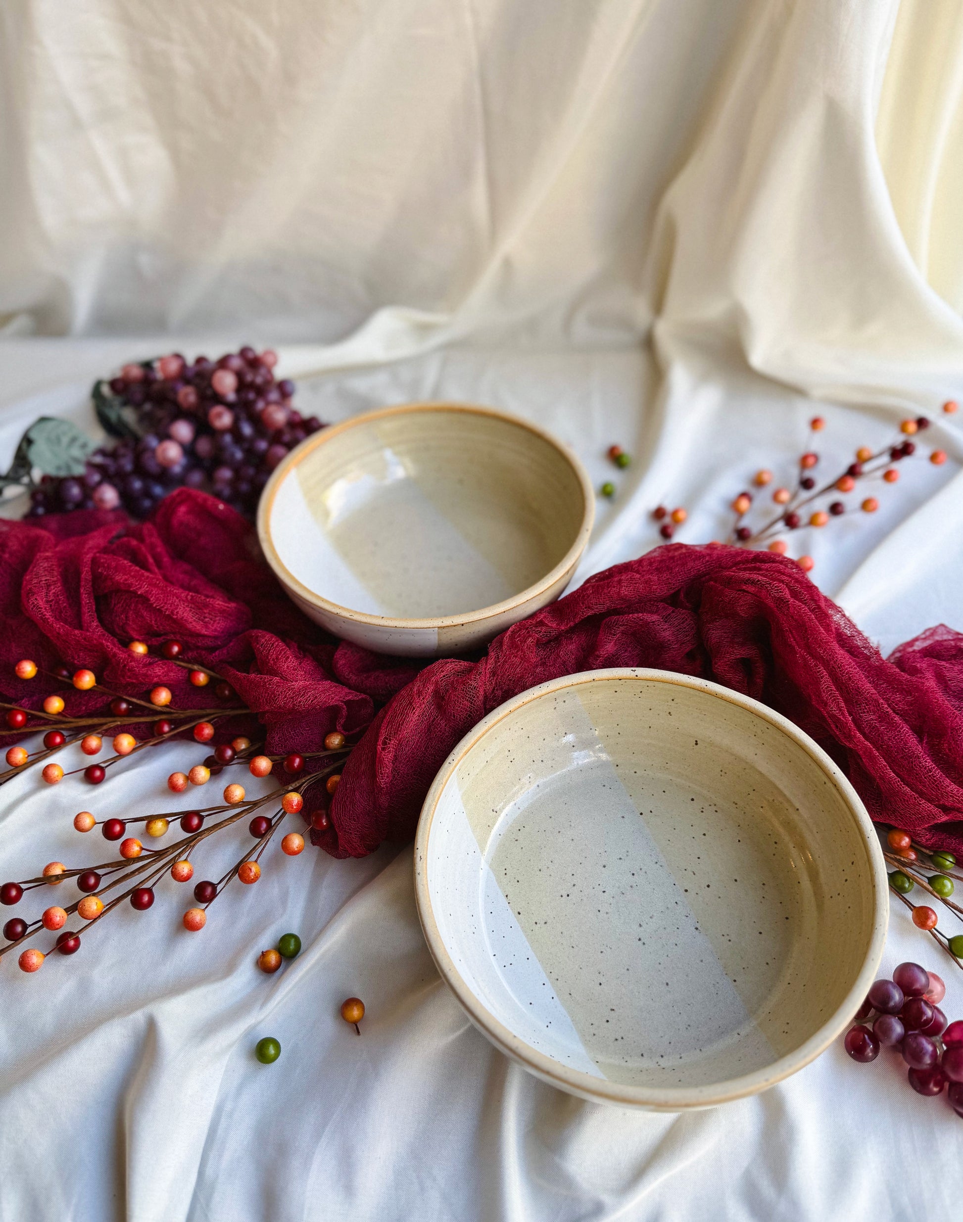 Two ceramic bowls on a white fabric background with red fabric and berries.